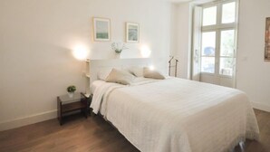 A bedroom with a bed, bedside tables, a nightstand, a window, and wall-mounted artwork. - Kensington by Interhome (La Croix-Valmer)