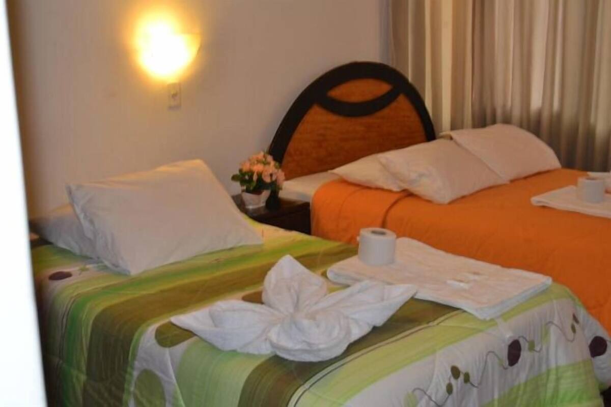 A hotel room with two beds, a nightstand with a lamp, and a flower vase.