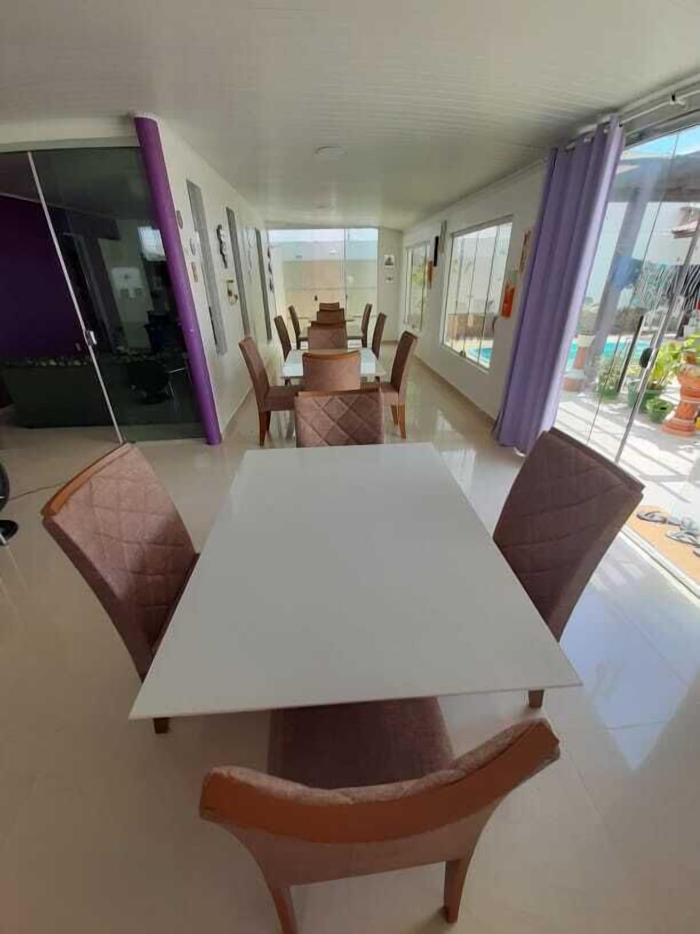 A spacious dining area with a large table and chairs, large windows, and a view of the outdoors.