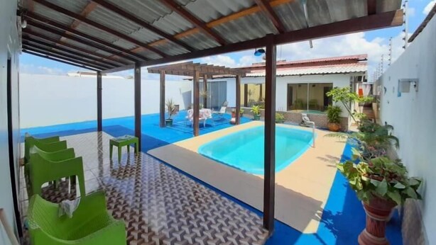 Un espacio exterior cubierto con piscina, sillas verdes y plantas en macetas.