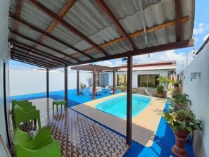 A covered outdoor area with a pool, green chairs, and potted plants. - Hostel Airla (Boa Vista)