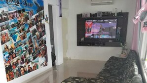 Una sala de estar con un sofá, un sillón mecedor de madera, un televisor montado en la pared y una composición de fotografías.