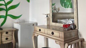 Una habitación compacta con escritorio de madera, espejo, refrigerador pequeño y cesto de basura.