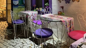 Un espacio al aire libre con mesas, sillas, un mural y plantas decorativas.