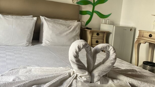 Habitación de hotel con cama, almohadas blancas, una presentación de toallas, aire acondicionado de pared y una mesita de noche con lámpara.