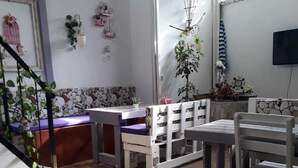 Una habitación con suelo de baldosas de piedra, muebles blancos y varios objetos decorativos, como plantas y cuadros.