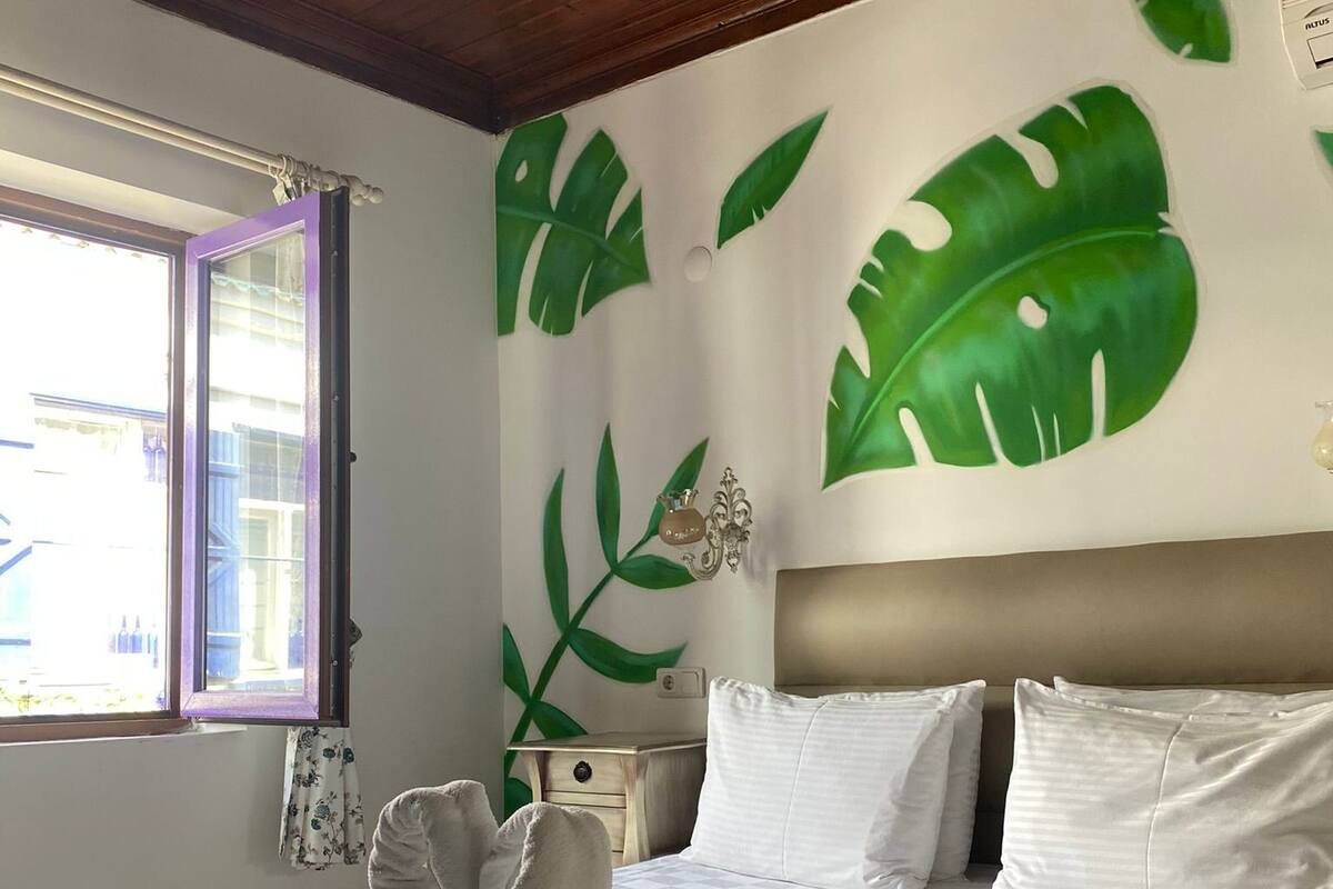A bedroom with a bed, a nightstand, a wall-mounted lamp, and a window with a view of the outside.