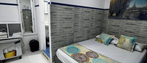 Quarto com cama, um quadro na parede e banheiro com cortina de chuveiro.