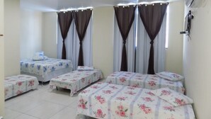 Una habitación con cuatro camas, cada una con ropa de cama de estampado floral. Hay cortinas en las ventanas y un equipo de aire acondicionado montado en la pared.