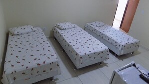 Una habitación con tres camas individuales, cada una con colcha de estampado floral. Las paredes son blancas y el piso está cubierto de baldosas. Se ve una puerta al lado derecho de la imagen.