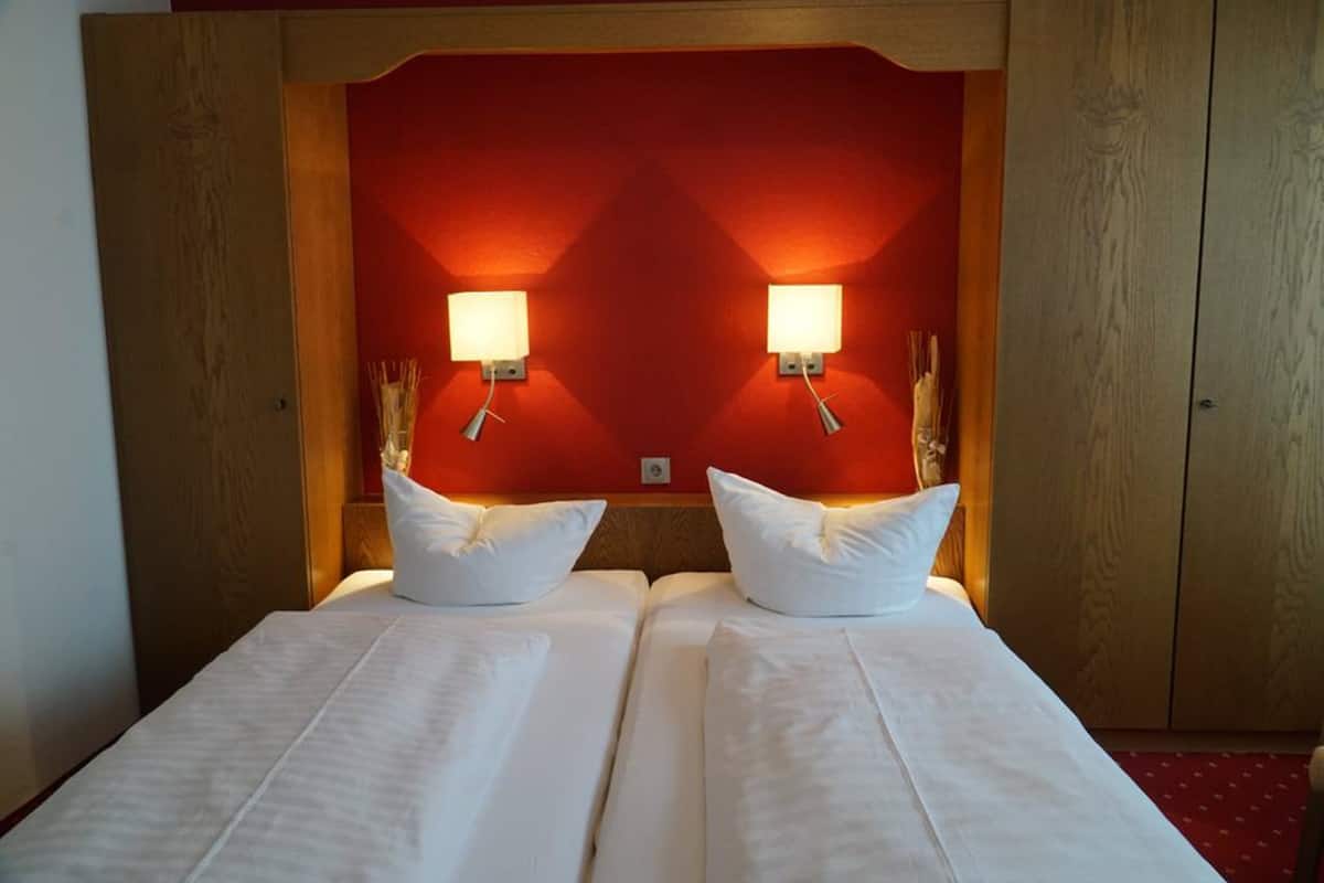 Habitación de hotel con dos camas, una pared de acento roja y lámparas fijadas a la pared.