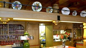 Een houten bar met een toog, planken met flessen en een decoratieve bordenopstelling aan het plafond.