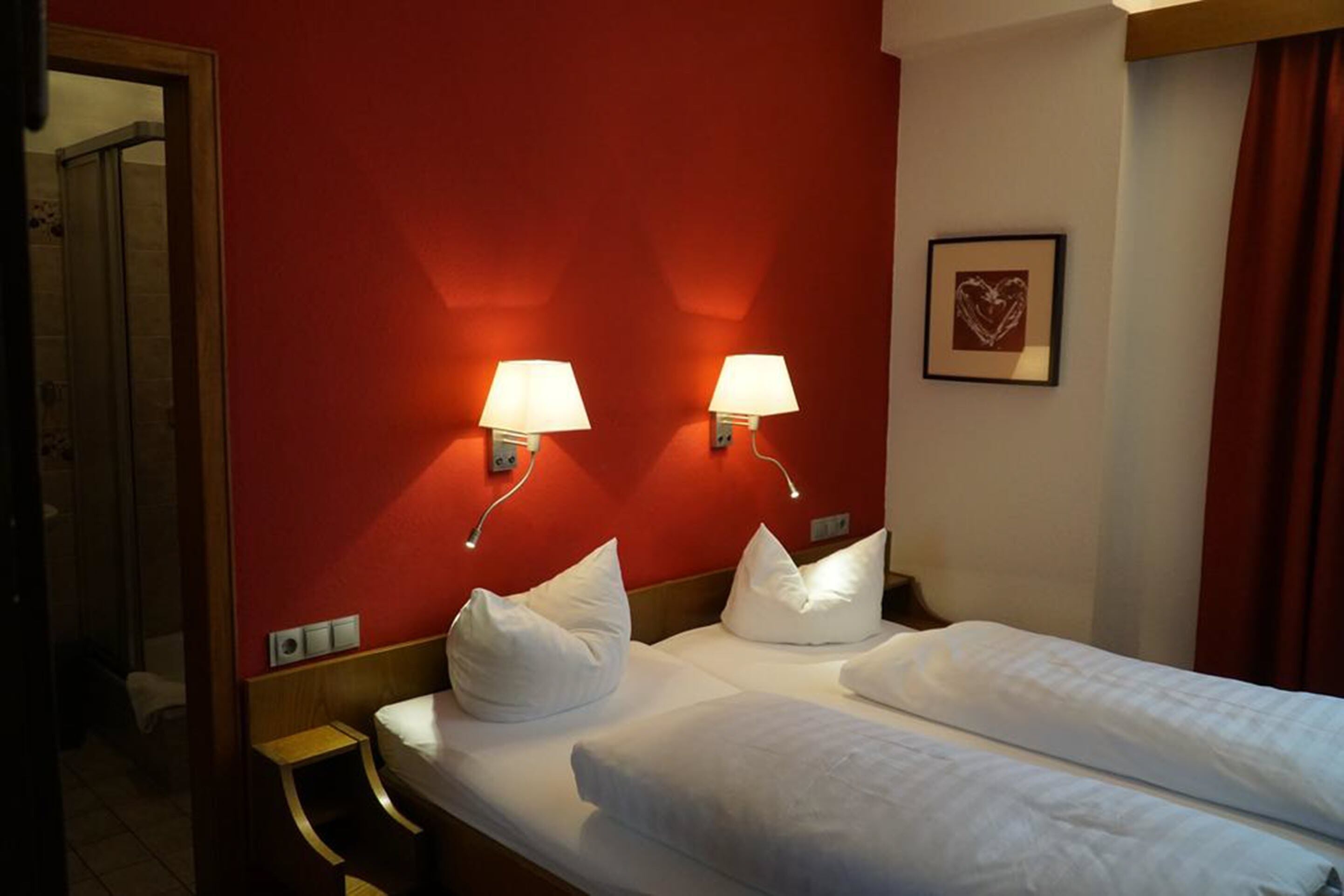 A hotel room with two beds, a red accent wall, and wall-mounted lamps.