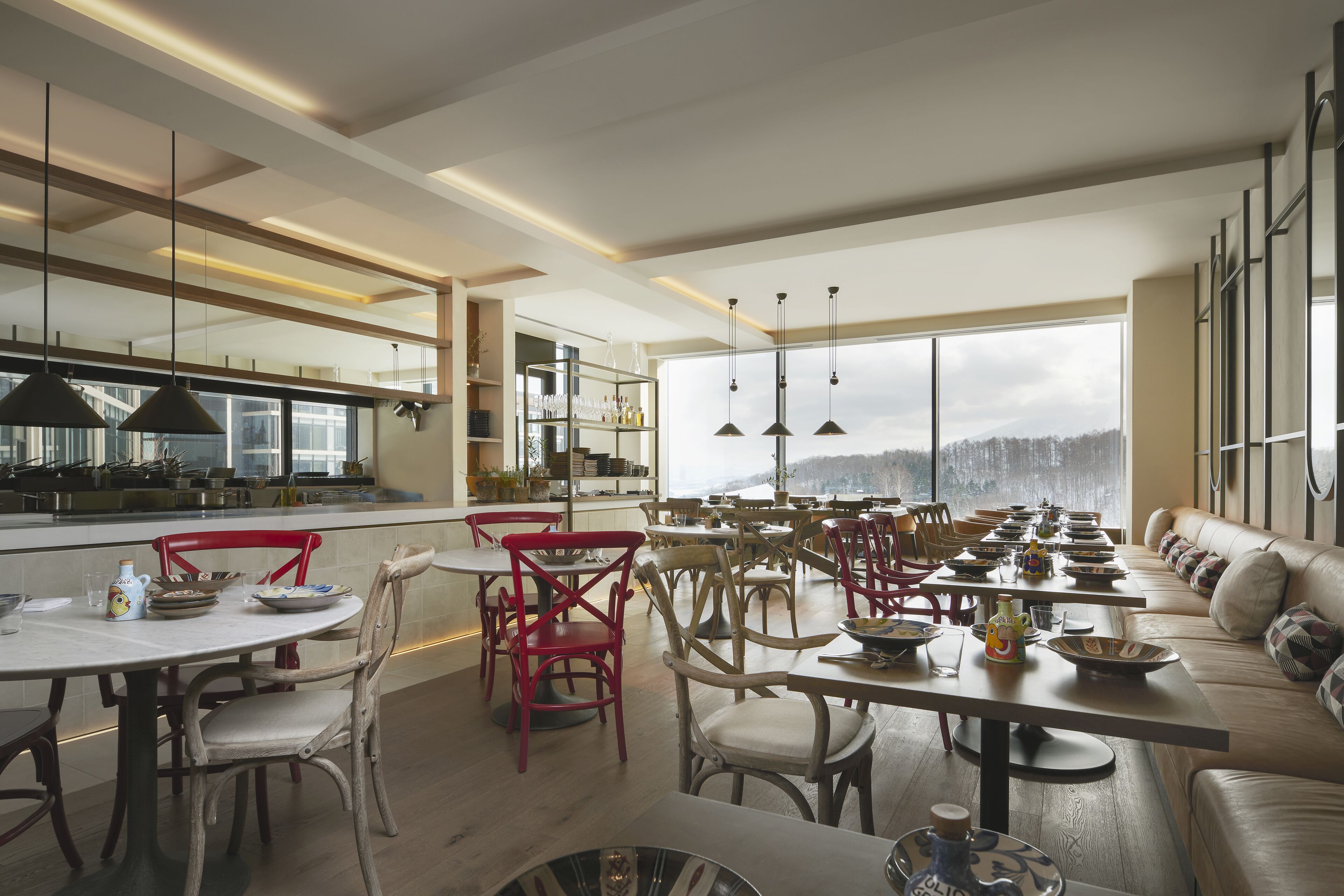 Un comedor amplio con múltiples mesas y sillas, una cocina equipada con electrodomésticos modernos, y ventanas grandes que ofrecen vistas al exterior.