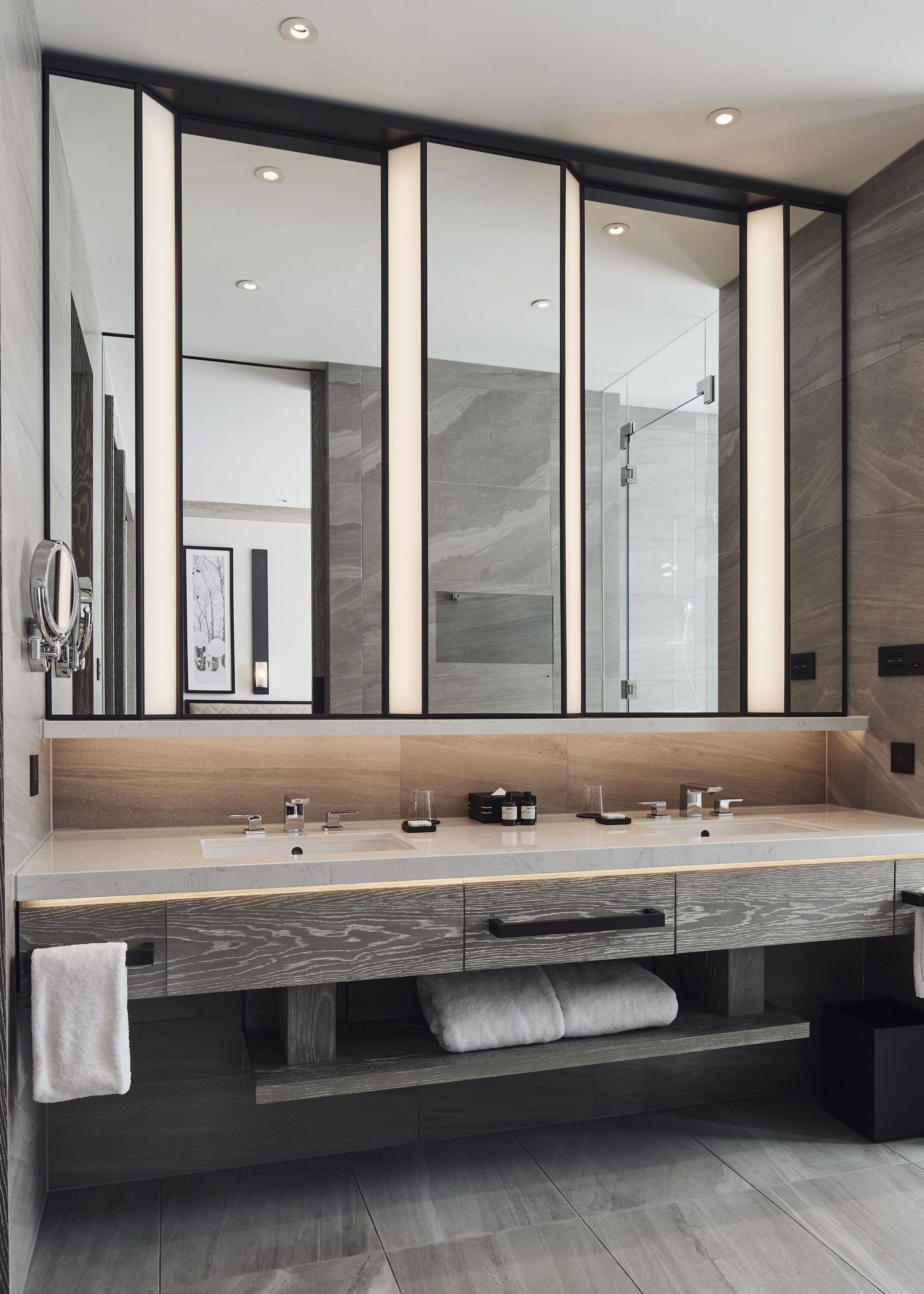 A modern bathroom with a large mirror, two sinks, and a shower.