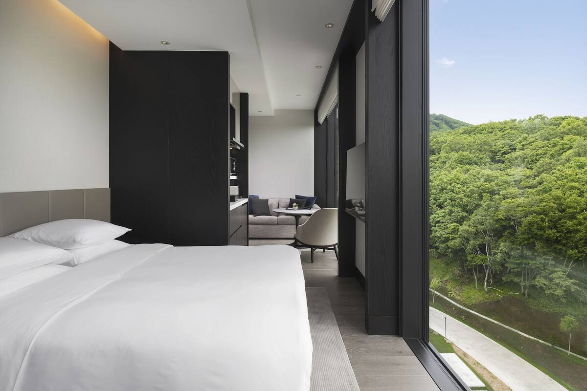 Ein modernes Hotelzimmer mit einem großen Bett, einem Schreibtisch und Blick auf einen üppigen Wald.