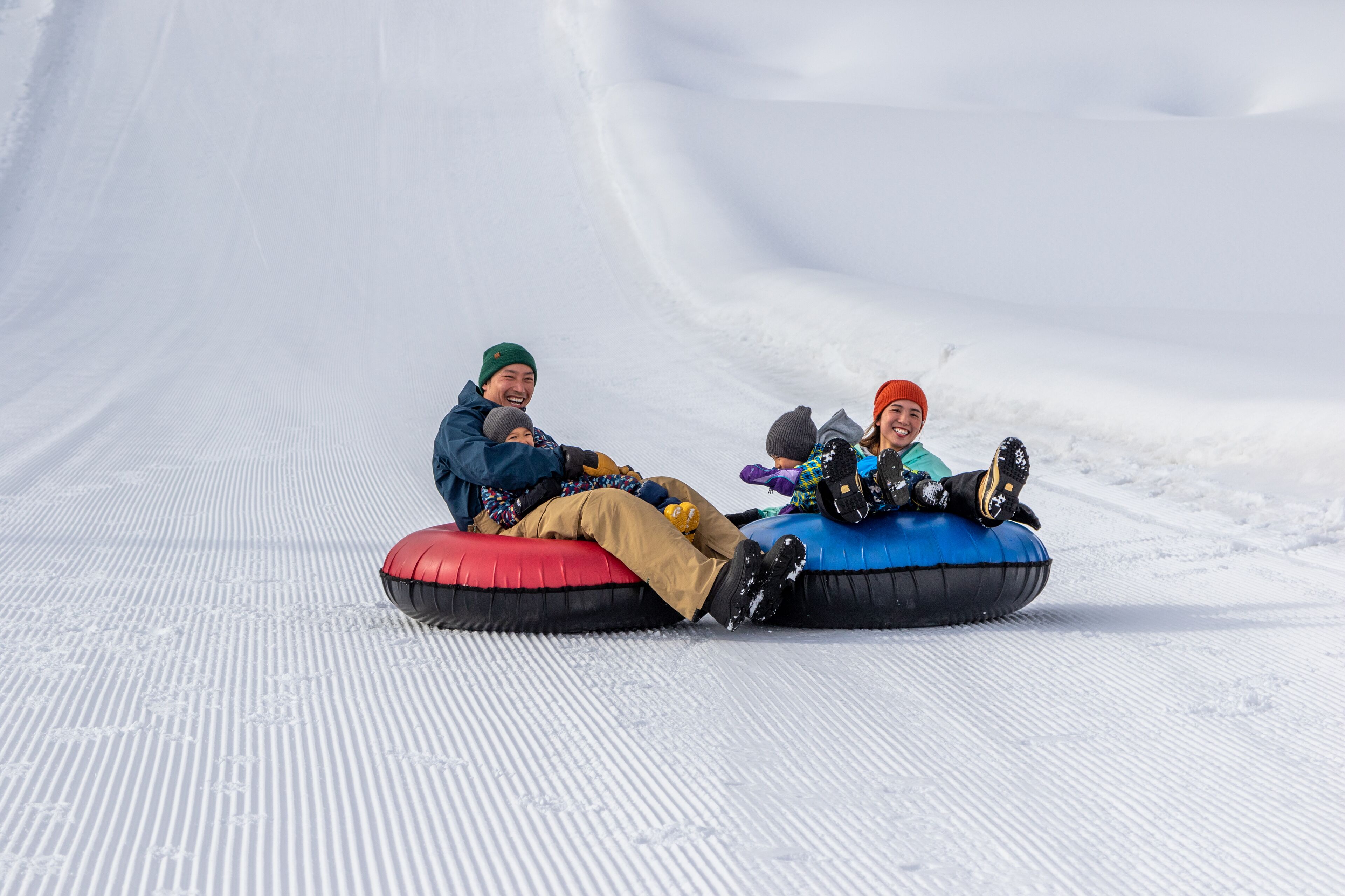 Dos personas en flotadores de nieve deslizándose por una pendiente nevada.