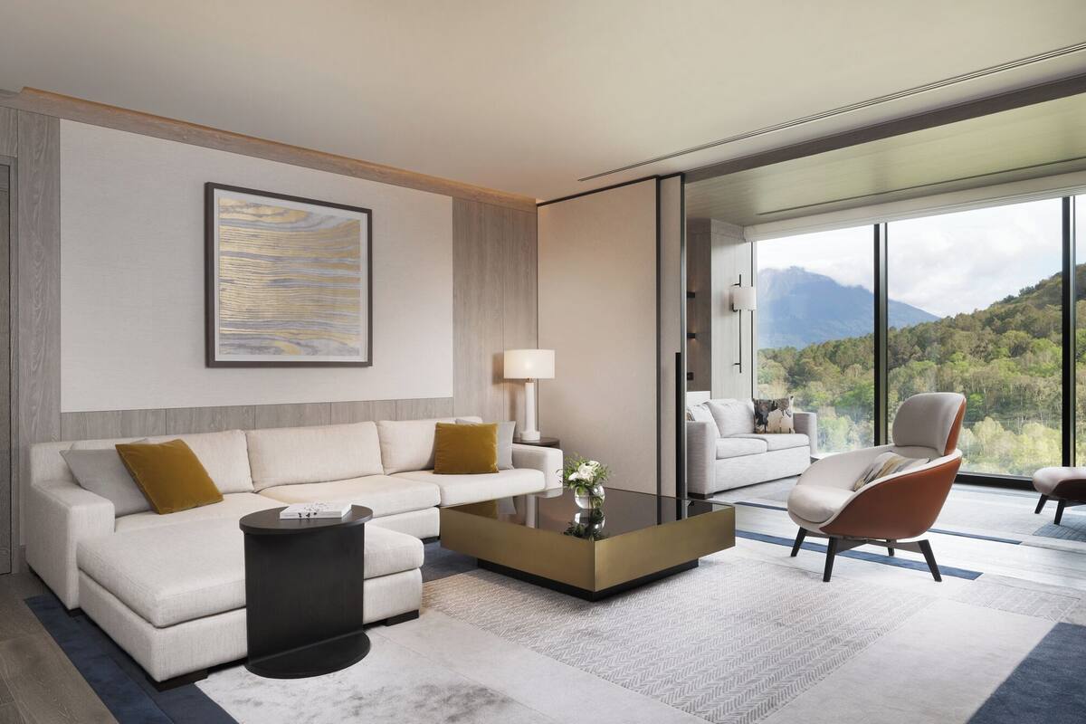 Ein modernes Wohnzimmer mit Sofa, Sessel, Couchtisch und einem großen Fenster mit Blick auf die Berge.