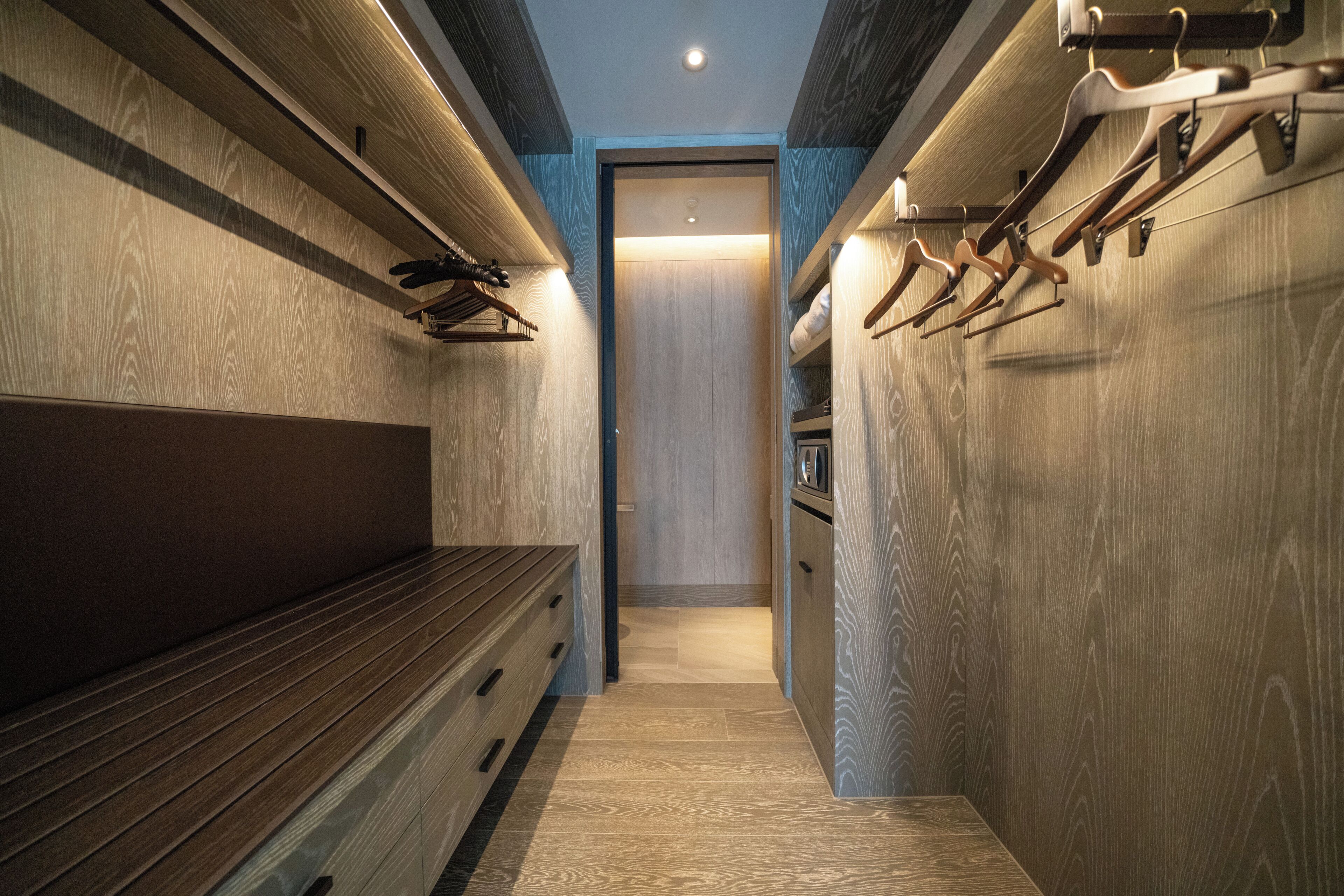 A narrow hallway with wooden paneling, a bench, and wooden hangers on the walls.
