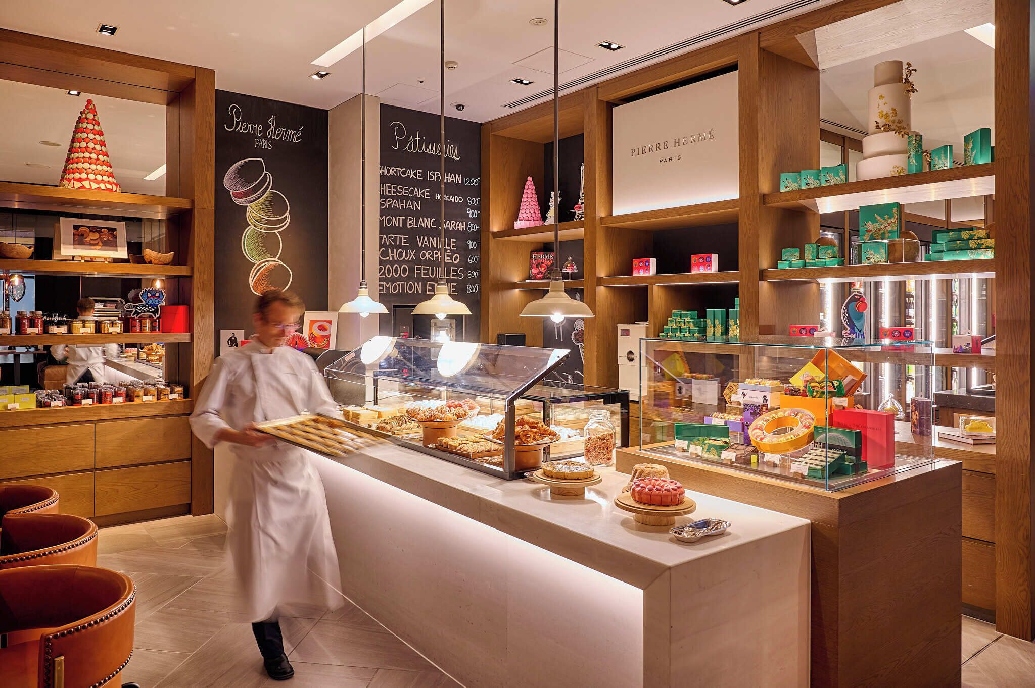 Un comptoir de boulangerie avec des pâtisseries, un menu écrit à la craie et des étagères en bois.
