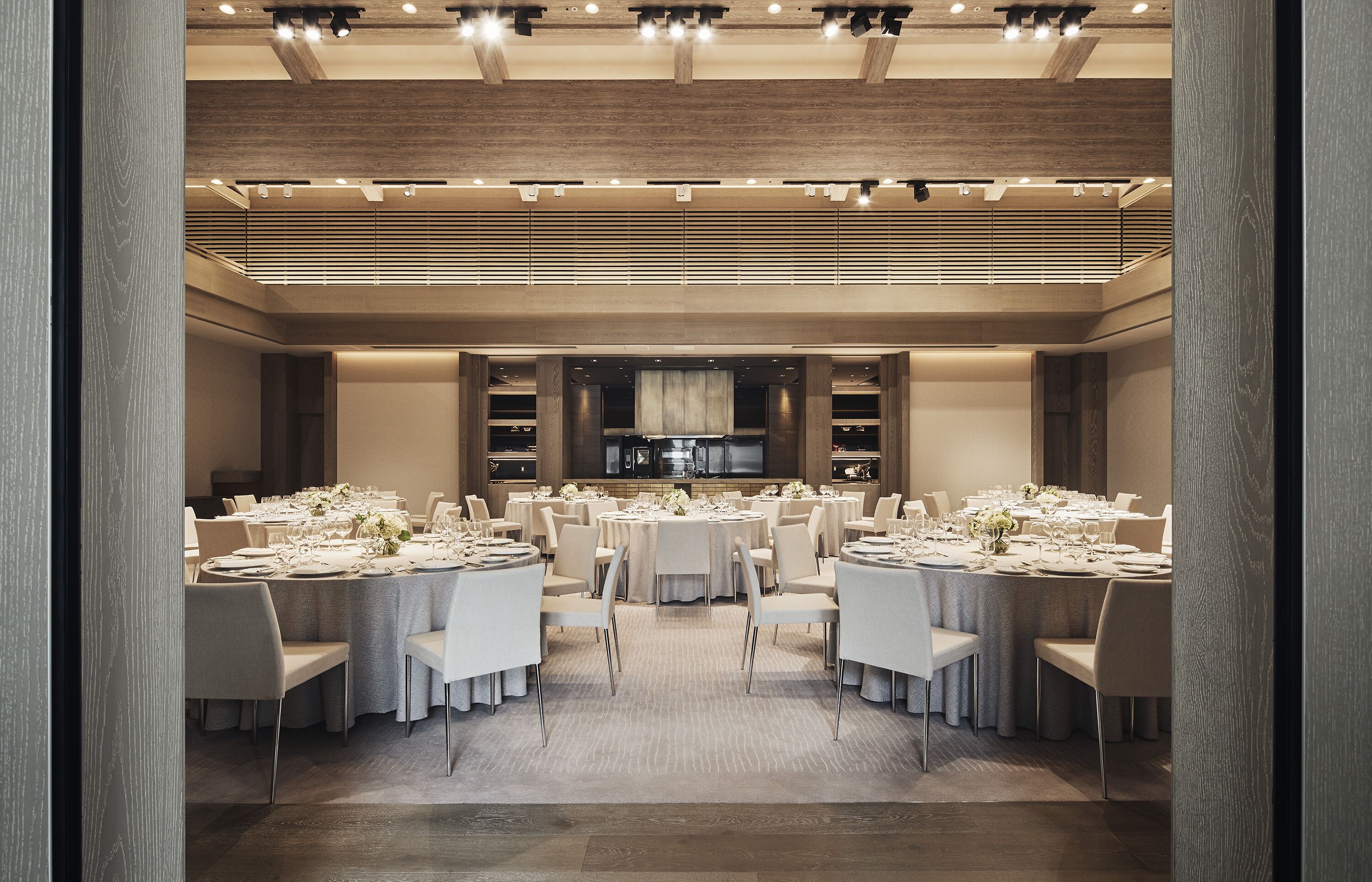 A spacious dining area with multiple round tables set for a formal event, featuring white tablecloths and elegant floral centerpieces.