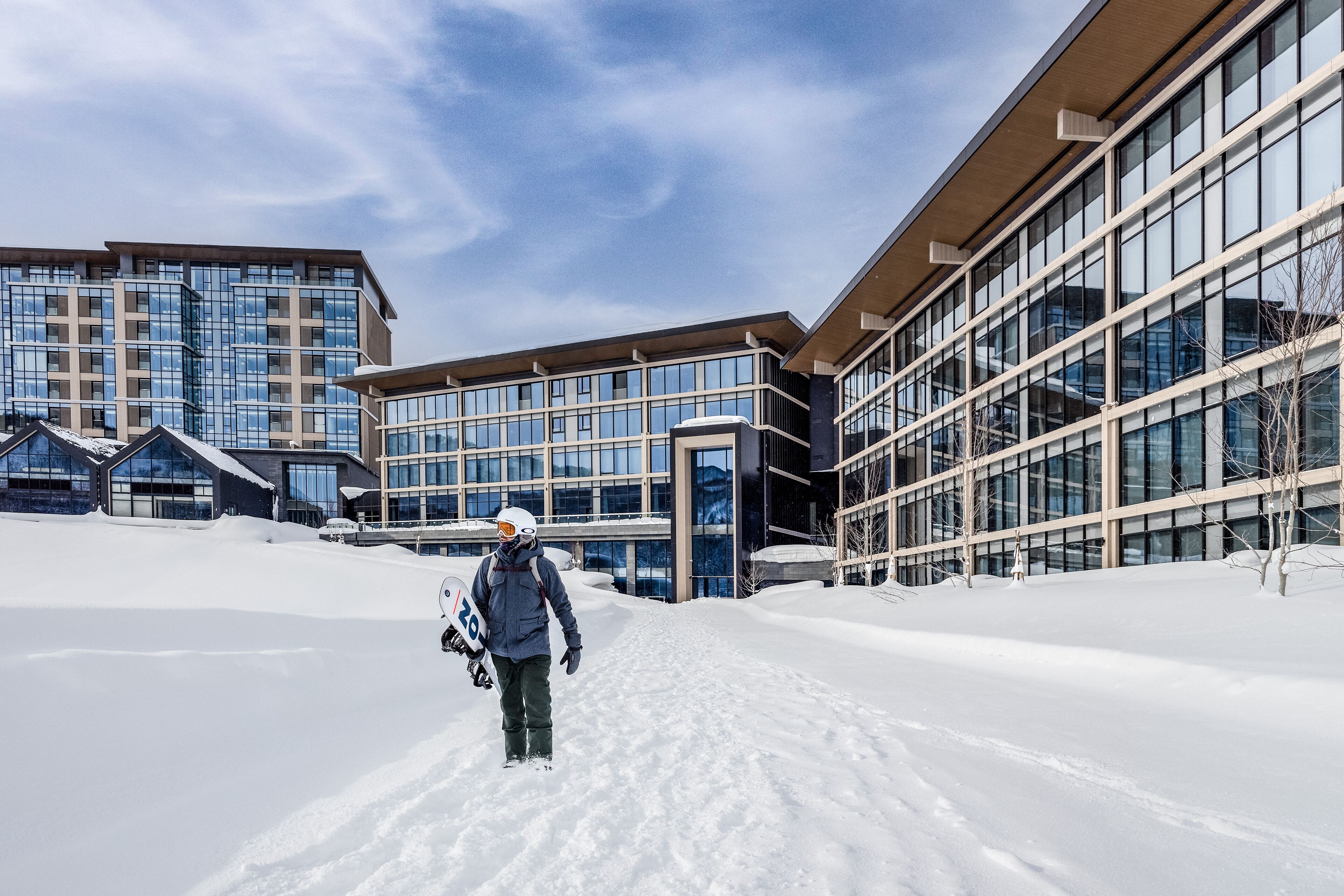 A person walking on a snow-covered path towards a modern building with large windows and a flat roof.