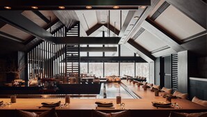 A modern dining area with a long table, multiple seating arrangements, and a high ceiling with skylights. - Park Hyatt Niseko Hanazono (Kutchan)