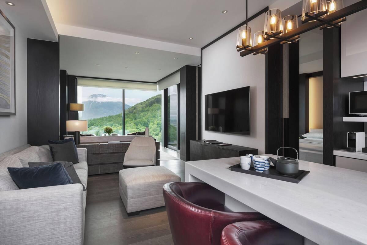 Ein modernes Hotelzimmer mit großem Fenster, Flachbildfernseher, Essbereich und einer Sitzecke.