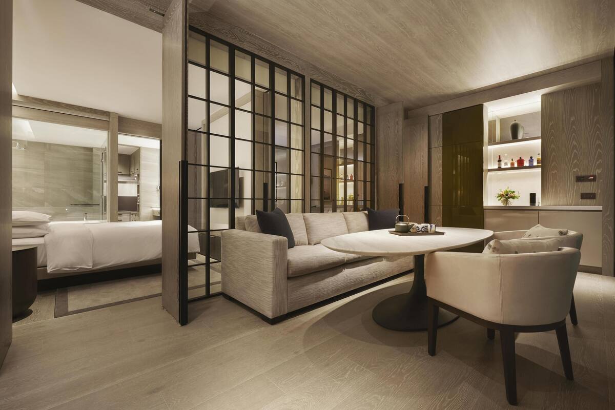 Ein modernes Hotelzimmer mit einer Couch, einem runden Tisch und Blick durch eine Glaswand.