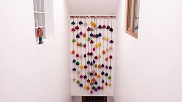 A staircase with a white wall, a colorful hanging decoration, and a window on the left.