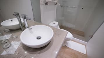Un baño moderno con dos lavabos, un inodoro y una cabina de ducha con mampara de vidrio.