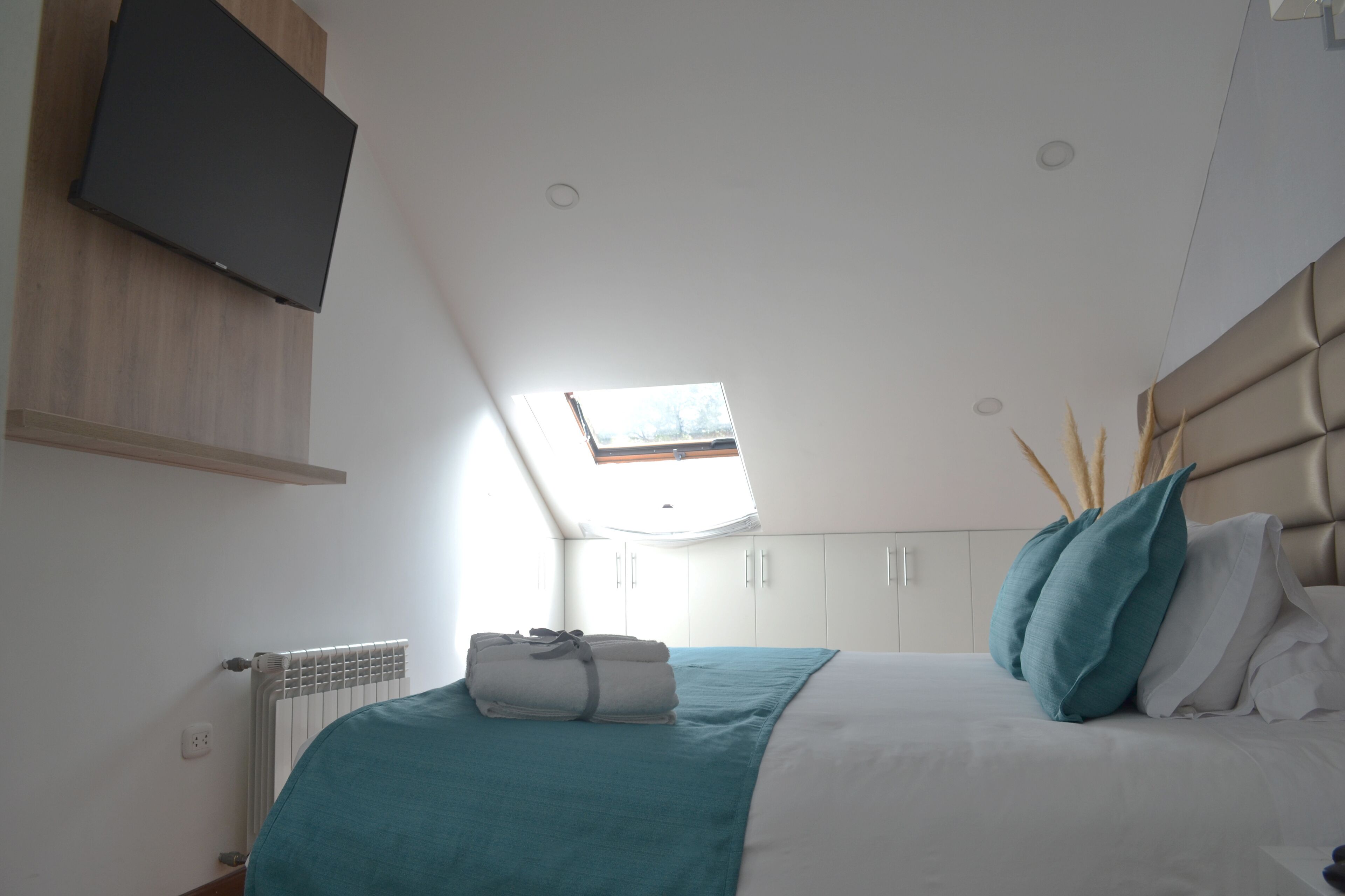 A bedroom with a bed, a TV mounted on the wall, a window, and a radiator.