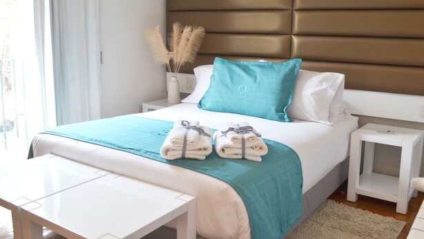 A neatly made bed with a teal and white bedspread, two folded towels on the bed, and a bedside table with a lamp.