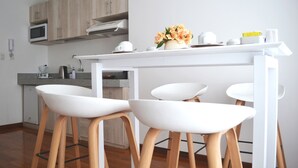A modern kitchen with wooden cabinets, a white countertop, and two white bar stools.