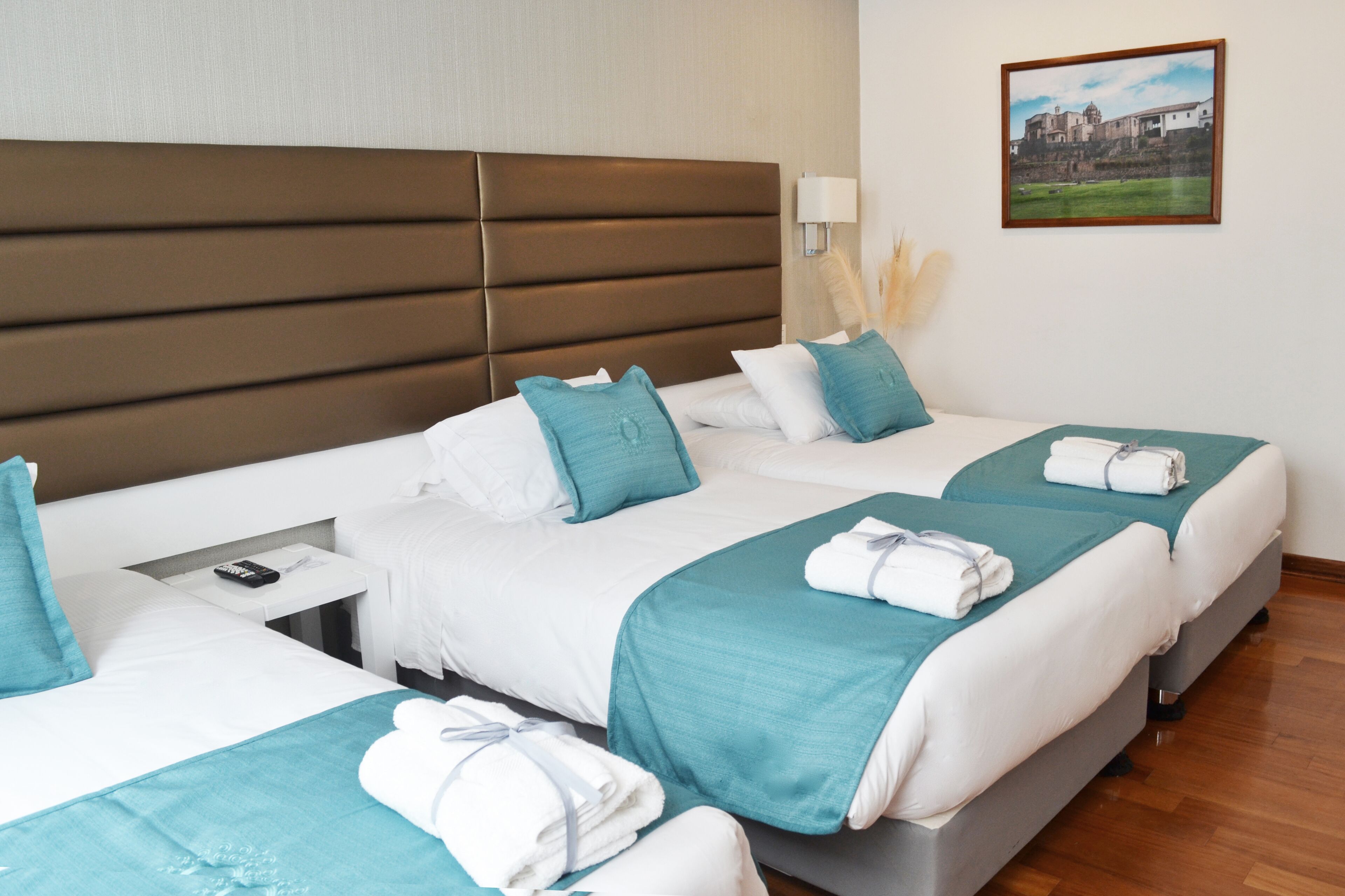 Habitación de hotel con dos camas, una mesita de noche, una lámpara y un cuadro en la pared.