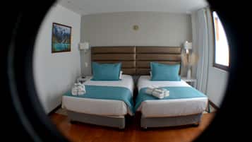 A room with two beds, each with a pillow and a blanket. There is a nightstand with a lamp and a phone on one side.