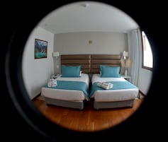 Una habitación con dos camas, cada una con una almohada y una manta. Hay una mesita de noche con una lámpara y un teléfono.