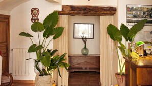 Un intérieur rustique avec des poutres apparentes, un lustre, des plantes en pot et une cheminée.