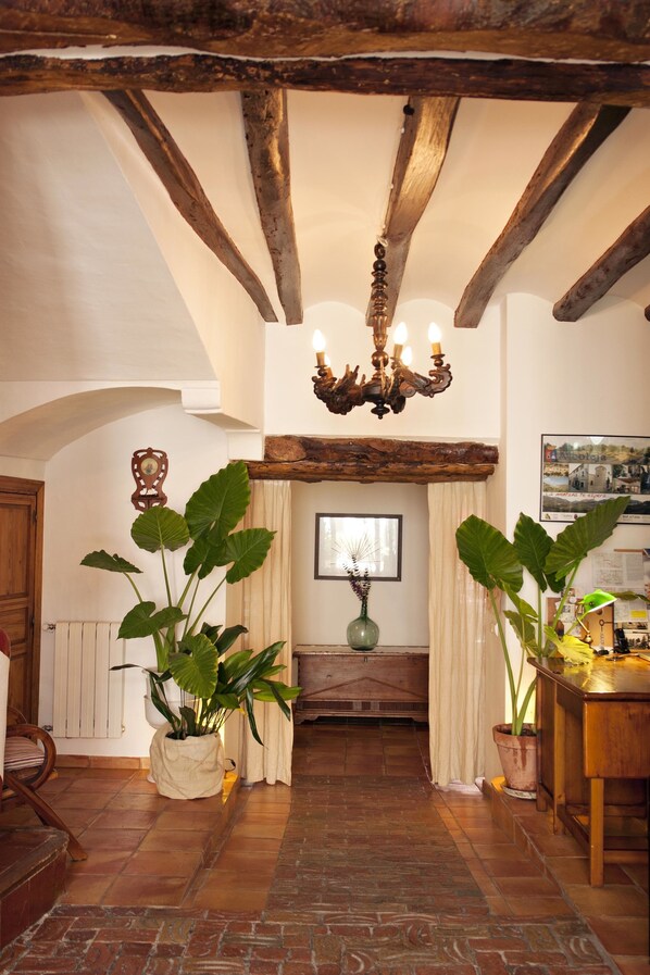 Un intérieur rustique avec des poutres apparentes, un lustre, des plantes en pot et une cheminée.
