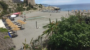 Una playa con sombrillas, mesas y una torre al fondo.