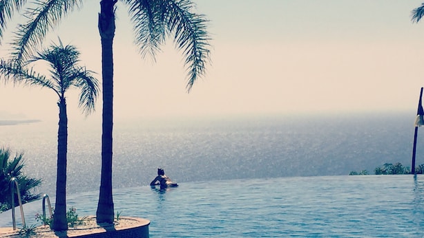 Una piscina con vistas al océano, palmeras y una persona en el agua.