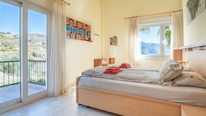 Un dormitorio con una cama grande, un ventanal con vistas a las colinas y un balcón.