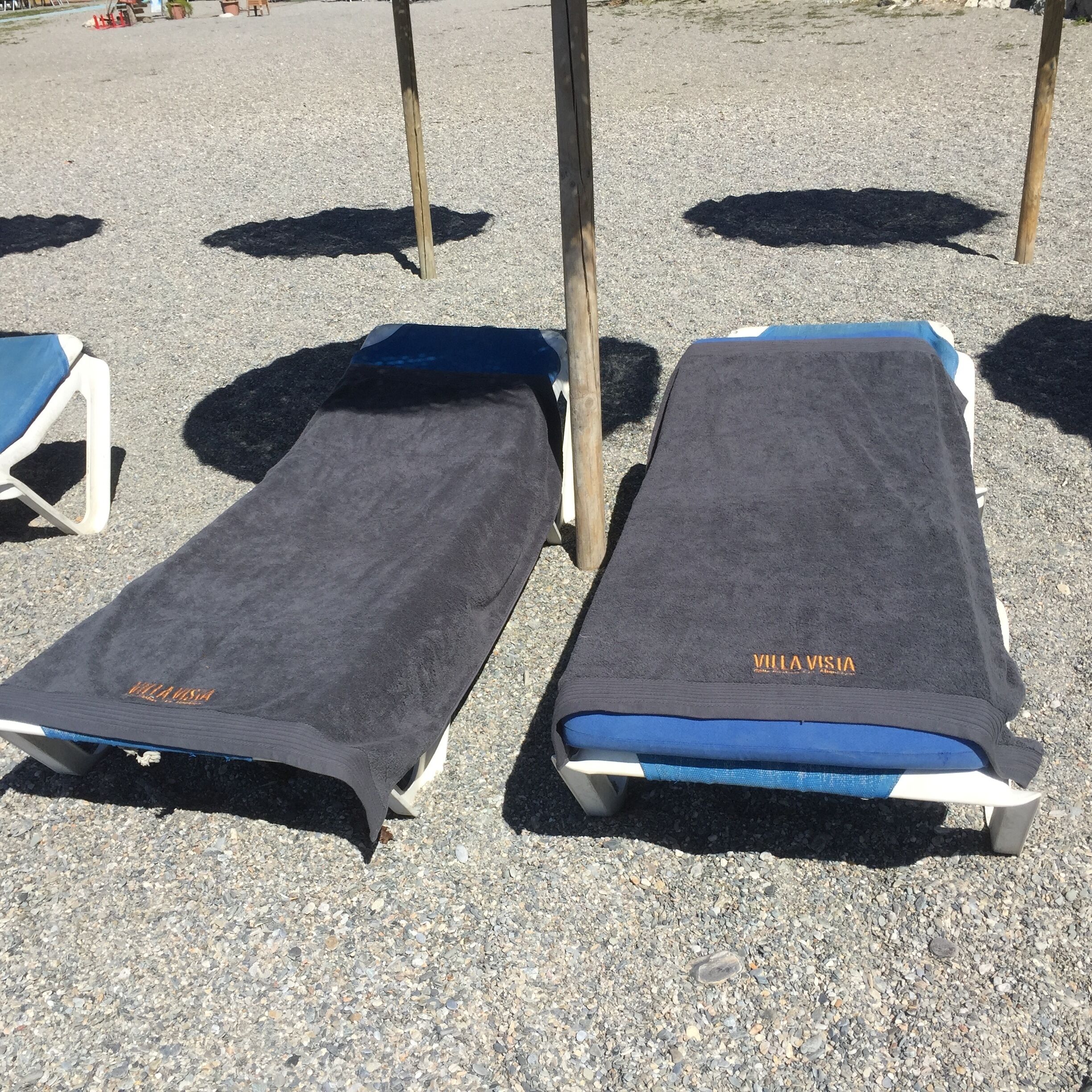 Two sun loungers with 'VIIVASIA' branding, positioned on a gravel surface with a clear sky in the background.