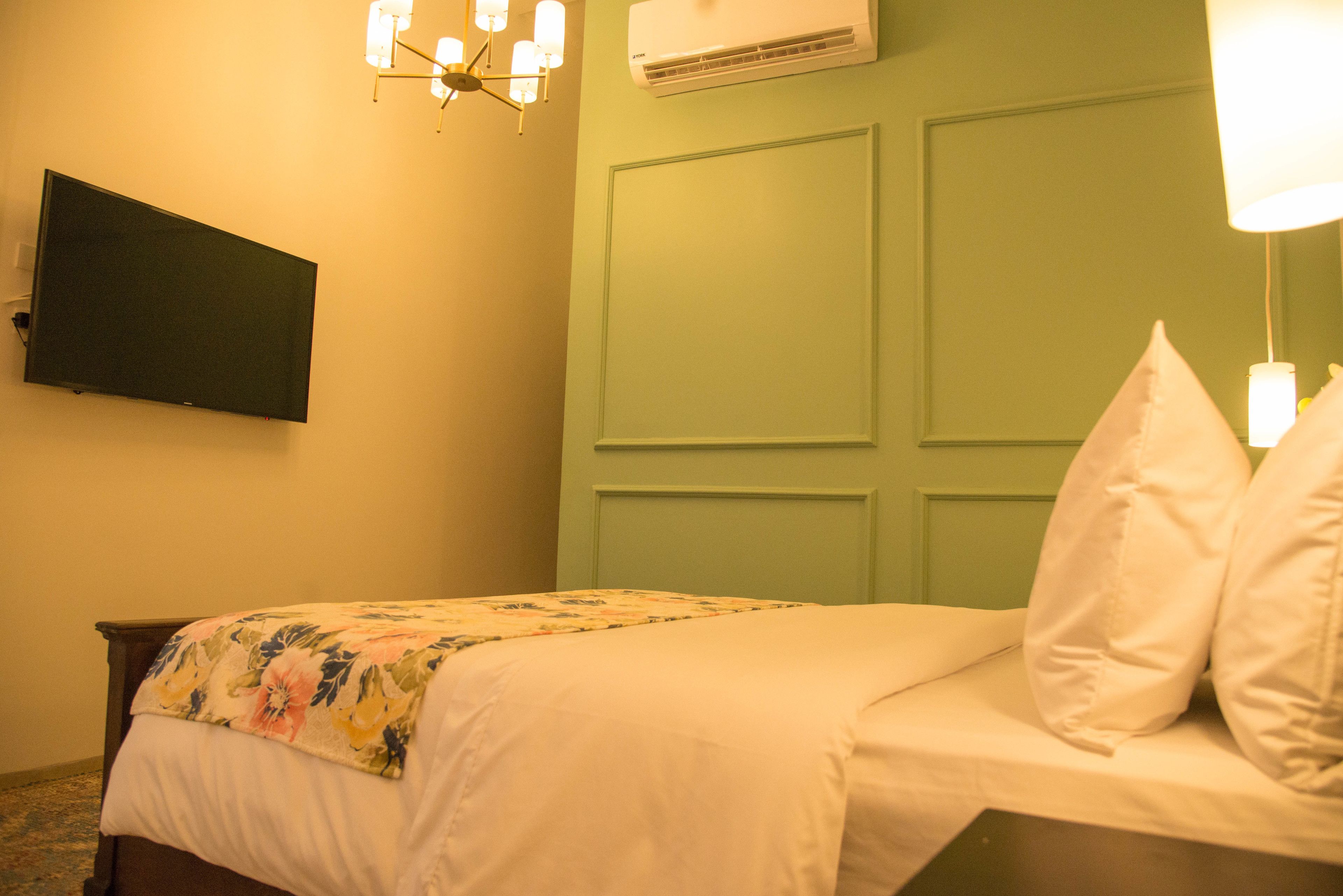 A bedroom with a bed, a flat-screen TV mounted on the wall, and an air conditioning unit above the bed.
