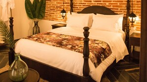 A hotel room with a brick-patterned wall, a four-poster bed, a small round table with a vase, and a hanging plant. - Soy Local Insignia (Cartagena)