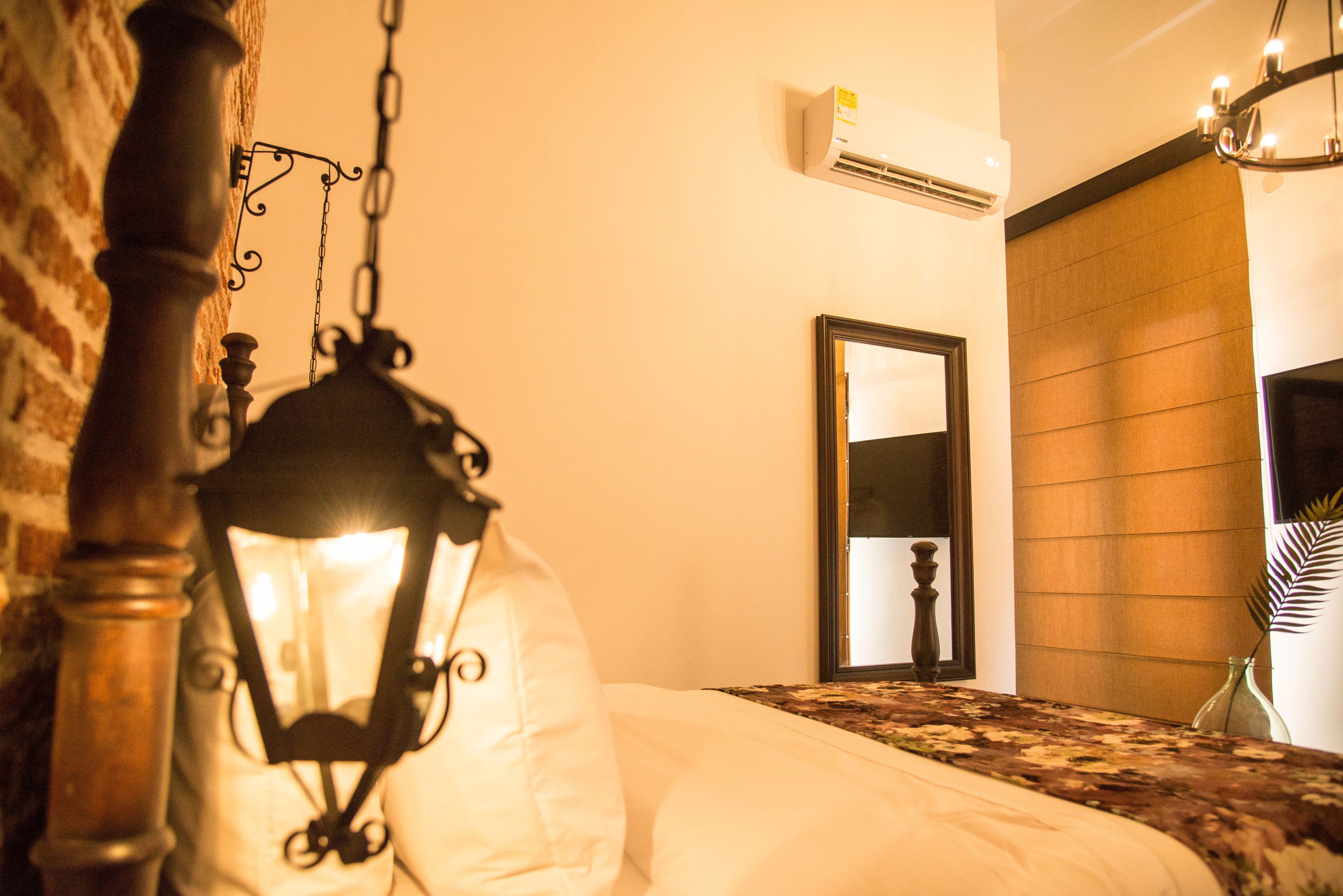 A bedroom with a bed, a hanging lamp, an air conditioning unit, and a mirror.