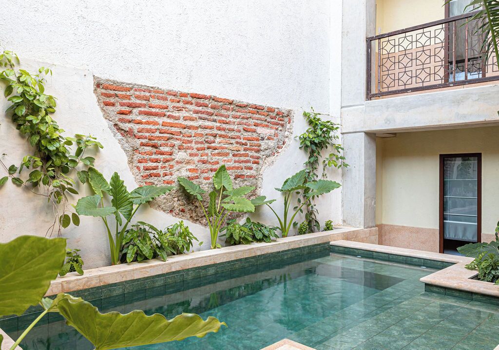 A pool area with a brick wall, plants, and a balcony with a geometric railing.