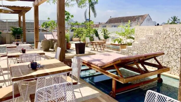 An outdoor pool area with lounge chairs and tables, surrounded by potted plants and a stone wall. - Soy Local Insignia (Cartagena)