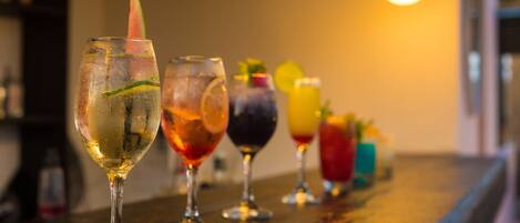 A row of colorful cocktails on a wooden bar counter.