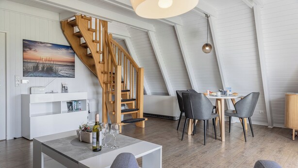 Een moderne loft met een houten trap, een eethoek met stoelen, en een witte console tafel met een fles en glazen.